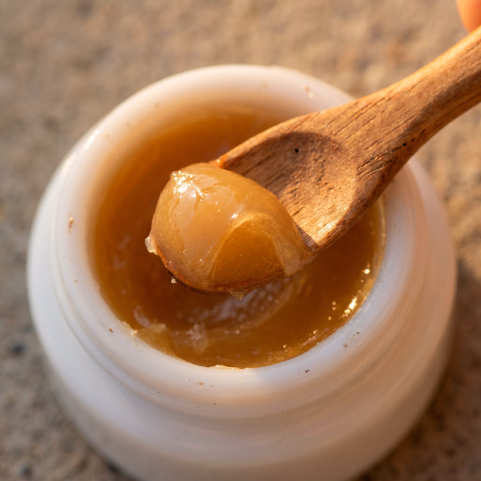 A scoop of warm-toned recovery balm — semi-translucent, photographed against bone-white porcelain.